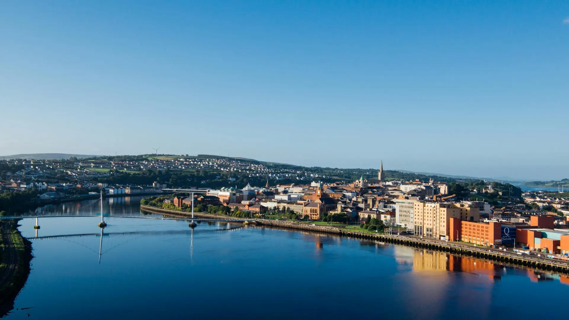 Aerial shot of Derry city and Peace Bridge over River Foyle at sunrise.