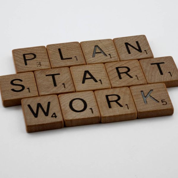 Wooden Scrabble tiles spelling 'Plan', 'Start', 'Work' on a white background.