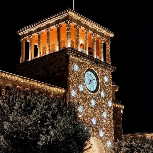 A brilliantly lit historic building with a clock tower adorned in festive lights, representing Yerevan's holiday spirit.