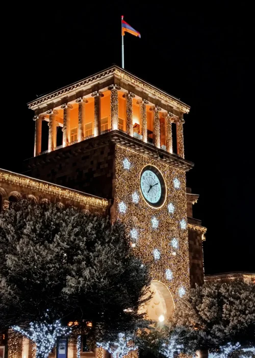 A brilliantly lit historic building with a clock tower adorned in festive lights, representing Yerevan's holiday spirit.